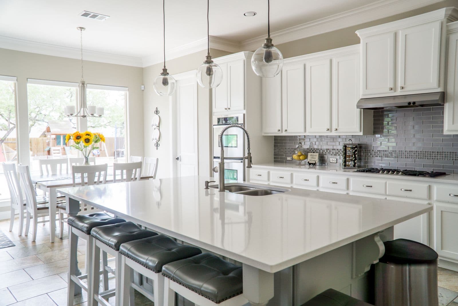 Remodeled kitchen with white cabinetry, quartz island with seating, and glass globe pendants